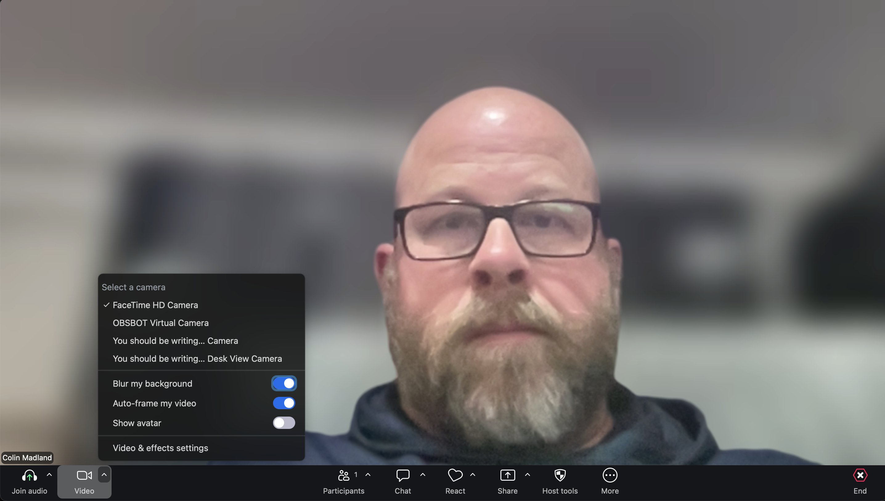 Colin in a Zoom session with his background blurred. The image shows where to toggle the blur on or off in the bottom left corner of Zoom