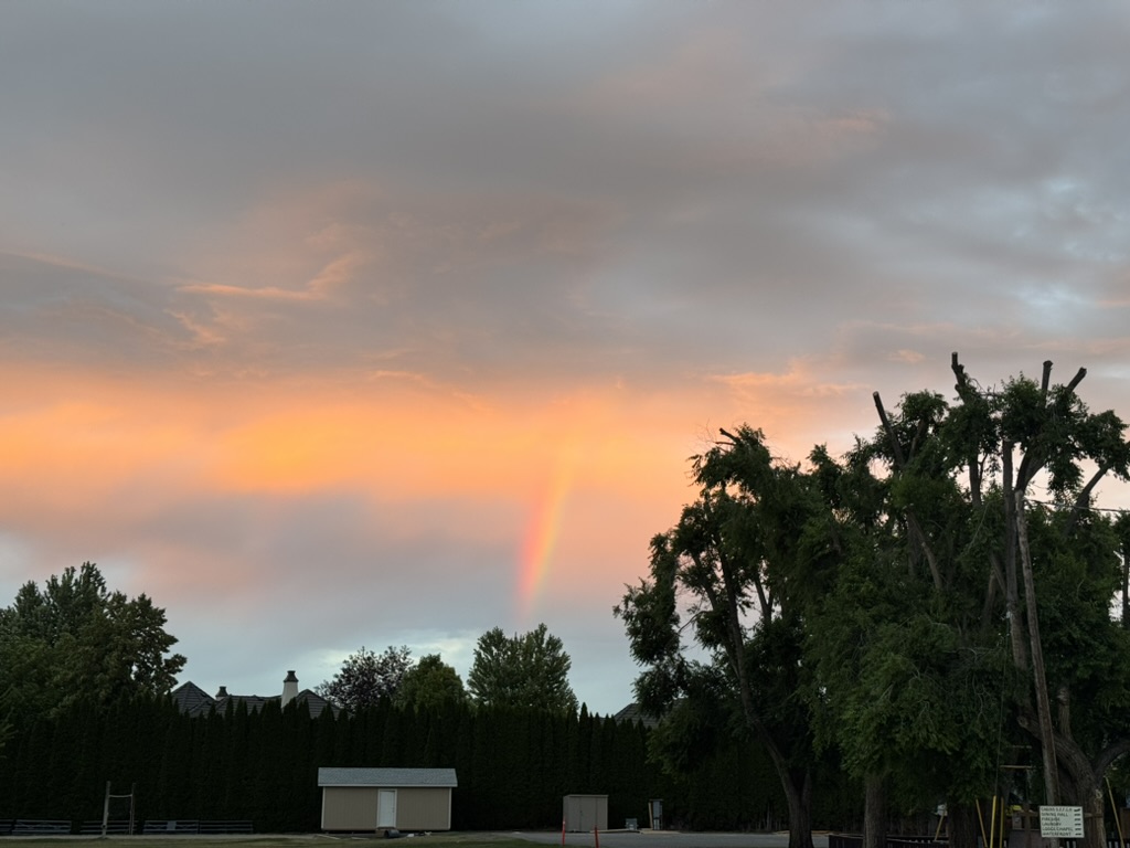 Sunsetty clouds glowing orange over Okanagan Lake and there's a rainbow visible in front of the sunset.